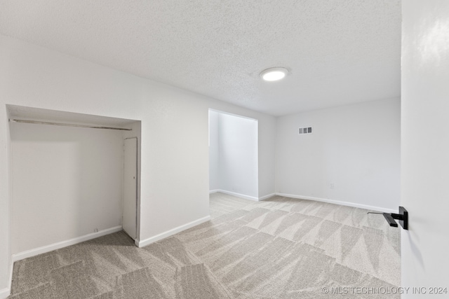 interior space with a textured ceiling, light colored carpet, and a closet