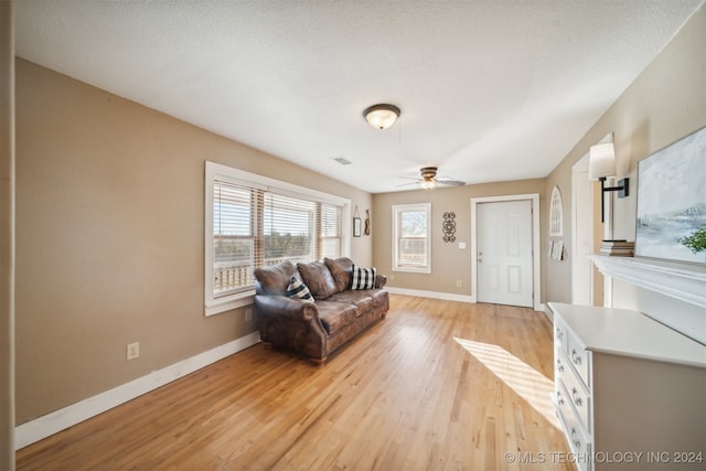 living room with ceiling fan, light wood-type flooring, and a textured ceiling