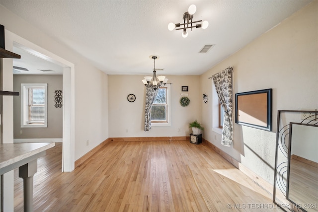 unfurnished dining area featuring a chandelier, a textured ceiling, light hardwood / wood-style flooring, and plenty of natural light