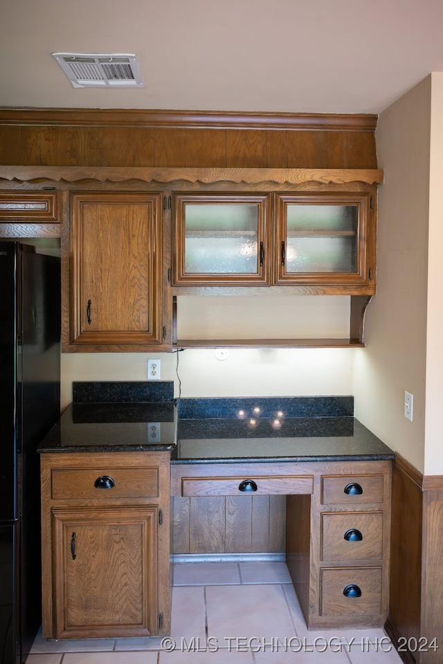 kitchen with dark stone countertops, black fridge, and light tile patterned floors