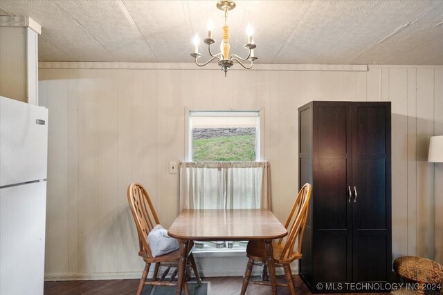 dining room with hardwood / wood-style flooring, wooden walls, and an inviting chandelier