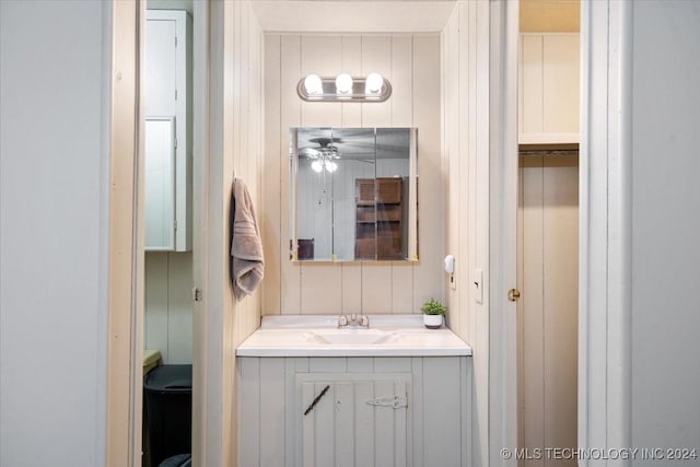 bathroom featuring vanity, toilet, ceiling fan, and wooden walls