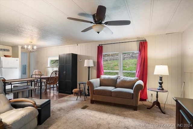 living room featuring carpet flooring, wooden walls, a textured ceiling, and ceiling fan with notable chandelier