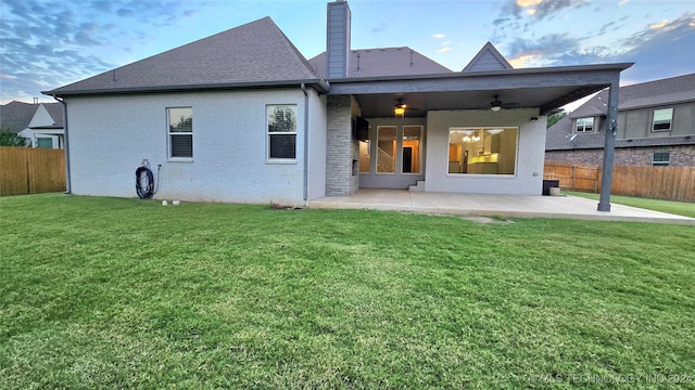 back house at dusk featuring a patio and a lawn