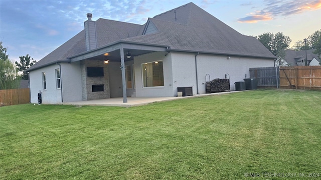 back house at dusk featuring a lawn and a patio area