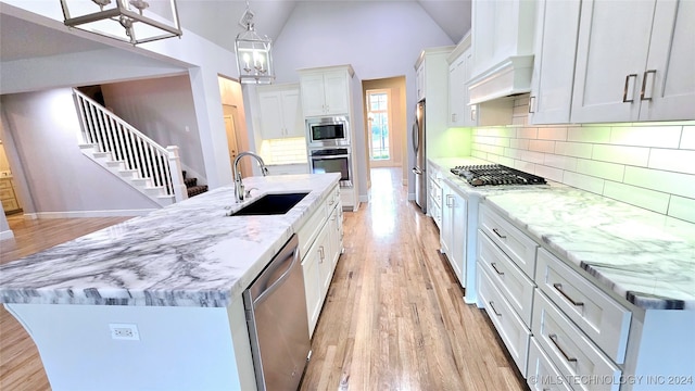 kitchen with hanging light fixtures, appliances with stainless steel finishes, white cabinets, light wood-type flooring, and vaulted ceiling