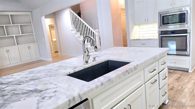 kitchen with light stone countertops, sink, stainless steel appliances, and light hardwood / wood-style floors