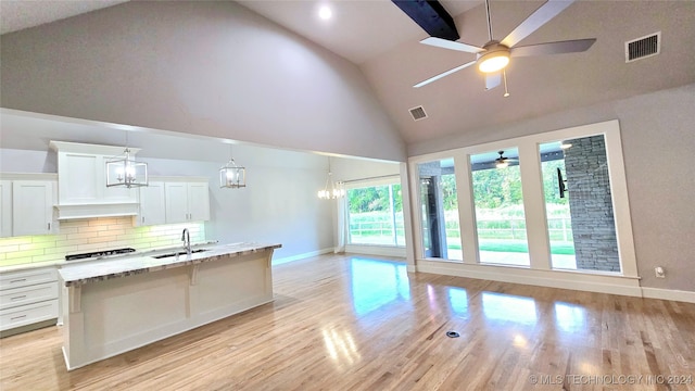 kitchen with tasteful backsplash, high vaulted ceiling, ceiling fan with notable chandelier, light hardwood / wood-style flooring, and sink