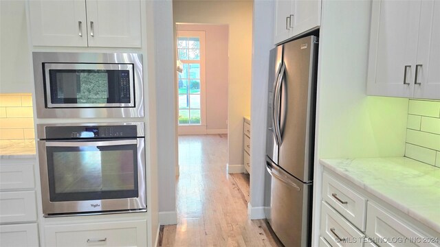 kitchen with appliances with stainless steel finishes, light wood-type flooring, white cabinets, and decorative backsplash