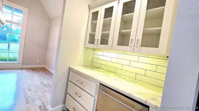 bar featuring light hardwood / wood-style flooring, white cabinets, dishwasher, light stone countertops, and backsplash