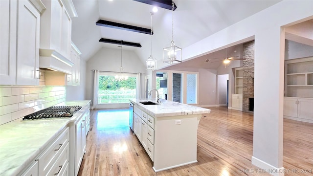 kitchen featuring ceiling fan with notable chandelier, decorative backsplash, white cabinets, a kitchen island with sink, and beamed ceiling