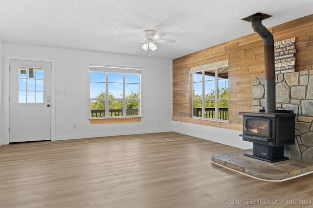 unfurnished living room featuring a wood stove, wooden walls, hardwood / wood-style floors, and ceiling fan