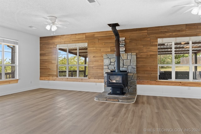 unfurnished living room with wood walls, plenty of natural light, and a wood stove