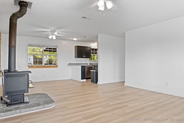 unfurnished living room featuring ceiling fan, a wood stove, a textured ceiling, and light hardwood / wood-style floors