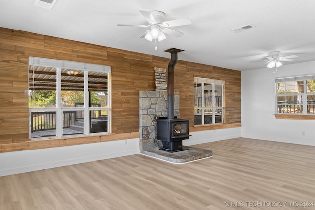 unfurnished living room featuring wood walls, a textured ceiling, a wood stove, and light hardwood / wood-style floors