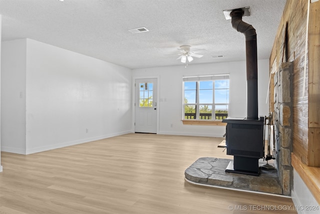 interior space with ceiling fan, a wood stove, a textured ceiling, and light hardwood / wood-style floors