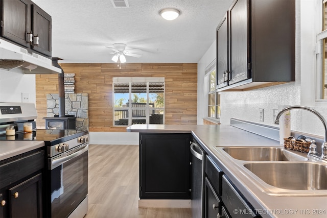 kitchen with a textured ceiling, ceiling fan, light hardwood / wood-style floors, wood walls, and stainless steel appliances