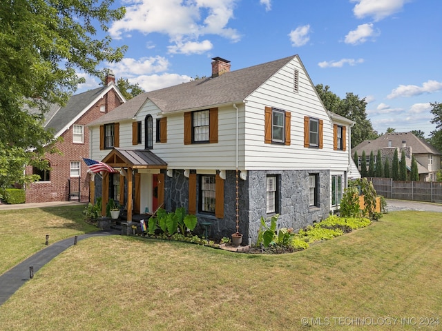 view of front of home featuring a chimney, a shingled roof, fence, stone siding, and a front lawn