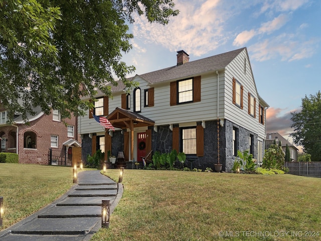 view of front of property featuring stone siding, a chimney, fence, and a front yard