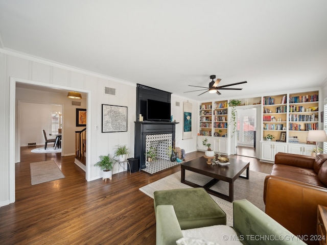 living room featuring built in shelves, dark wood-style flooring, crown molding, visible vents, and a ceiling fan