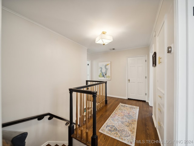 hall with dark wood finished floors, crown molding, and an upstairs landing