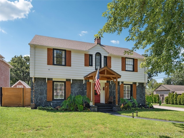 colonial home featuring a chimney, fence, and a front yard