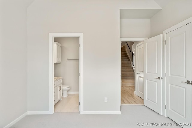 unfurnished bedroom featuring ensuite bath, baseboards, and light carpet
