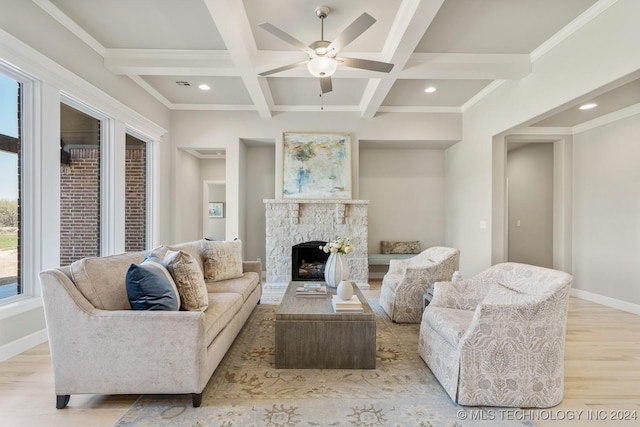 living room featuring light wood finished floors, a stone fireplace, beam ceiling, baseboards, and ceiling fan