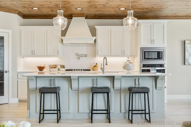 kitchen featuring appliances with stainless steel finishes, light wood-type flooring, custom exhaust hood, white cabinetry, and wooden ceiling