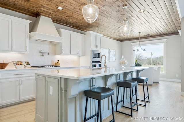 kitchen with a kitchen island with sink, wood ceiling, stainless steel appliances, premium range hood, and white cabinetry