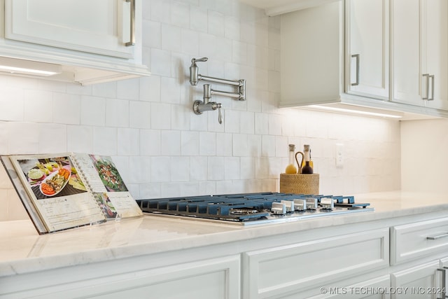 kitchen with light stone countertops, tasteful backsplash, stainless steel gas cooktop, and white cabinetry