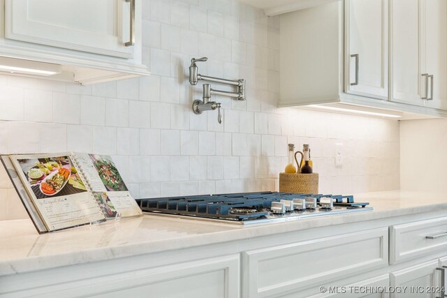 kitchen featuring backsplash, stainless steel gas cooktop, light stone countertops, and white cabinetry
