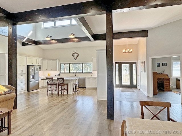 living room featuring beamed ceiling, a chandelier, light hardwood / wood-style flooring, sink, and a high ceiling