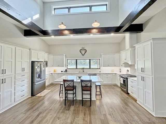 kitchen with appliances with stainless steel finishes, a kitchen island, sink, a towering ceiling, and light hardwood / wood-style flooring