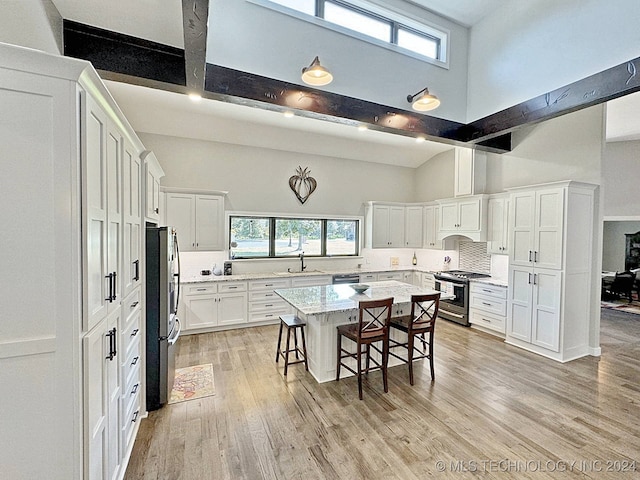 kitchen with stainless steel appliances, light hardwood / wood-style flooring, a towering ceiling, and a center island