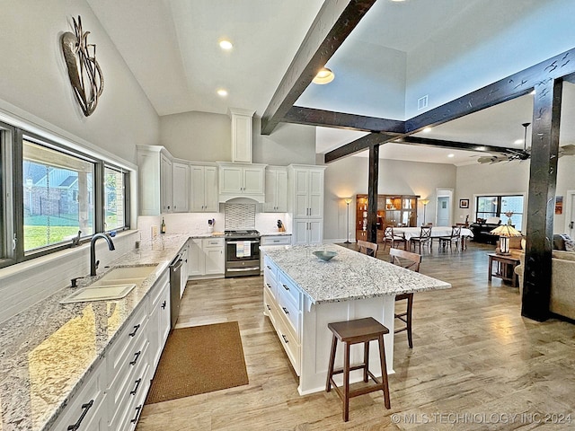 kitchen featuring appliances with stainless steel finishes, high vaulted ceiling, a kitchen island, and light stone countertops