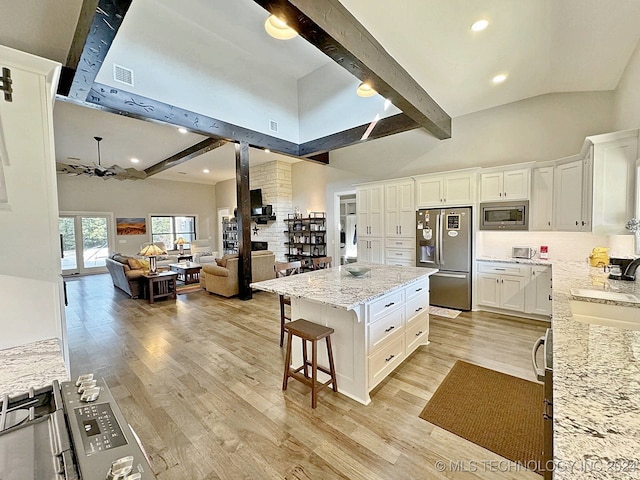 kitchen with appliances with stainless steel finishes, light hardwood / wood-style floors, white cabinetry, beam ceiling, and a center island