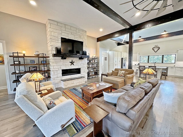 living room with beam ceiling, light hardwood / wood-style flooring, and a stone fireplace