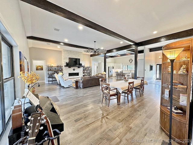 dining area with beam ceiling, light hardwood / wood-style flooring, a stone fireplace, and ceiling fan