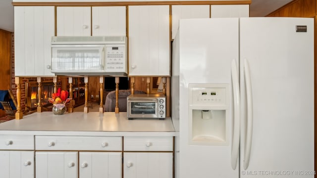 kitchen with a brick fireplace, white appliances, and white cabinetry