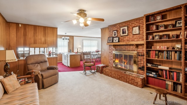 living room with a brick fireplace, ceiling fan with notable chandelier, wooden walls, and light carpet