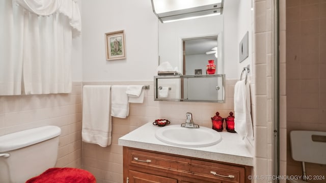 bathroom with tile walls, vanity, toilet, and a shower with door