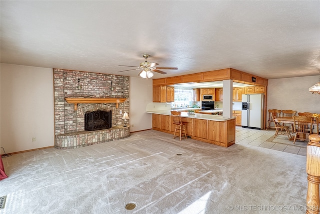 interior space featuring white refrigerator with ice dispenser, kitchen peninsula, stainless steel microwave, a fireplace, and ceiling fan