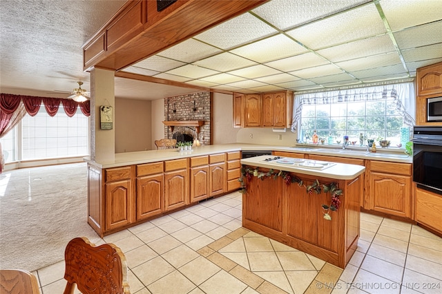 kitchen with kitchen peninsula, a kitchen island, light tile patterned floors, black oven, and ceiling fan