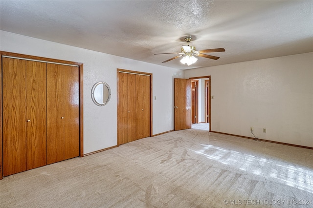 unfurnished bedroom featuring a textured ceiling, two closets, ceiling fan, and light colored carpet