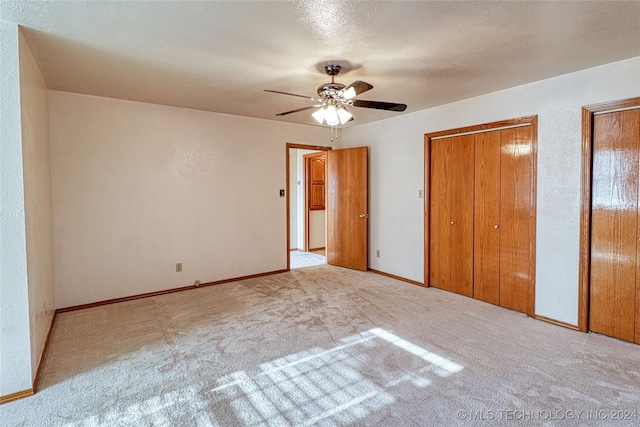 unfurnished bedroom with a textured ceiling, light carpet, ceiling fan, and multiple closets