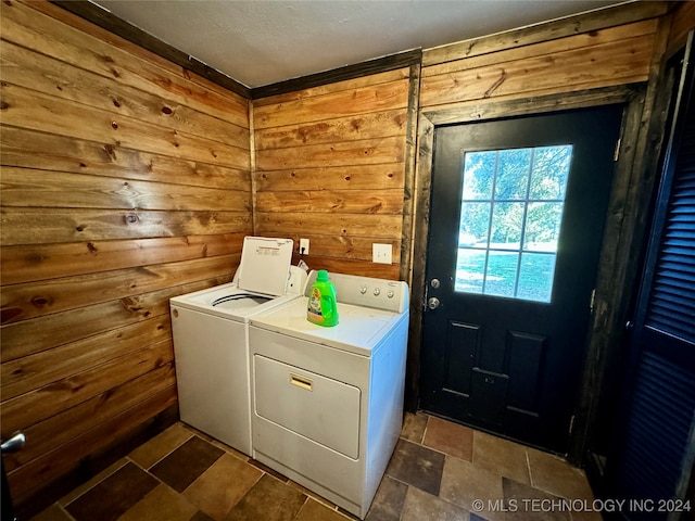 clothes washing area featuring wood walls, independent washer and dryer, and dark tile patterned floors