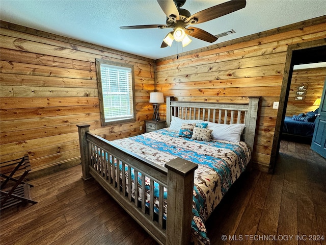 bedroom featuring ceiling fan, dark hardwood / wood-style flooring, a textured ceiling, and wooden walls