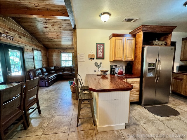 kitchen featuring light tile patterned floors, wood walls, lofted ceiling, and stainless steel fridge