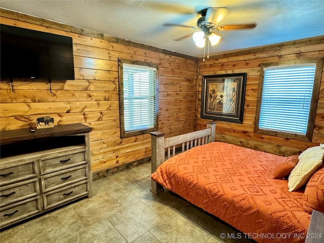 bedroom with ceiling fan, wood walls, and tile patterned floors